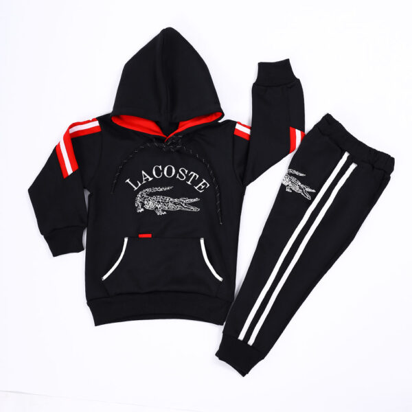 A black hooded sweatshirt and matching sweatpants set for boys, featuring the Lacoste crocodile logo and red accents.