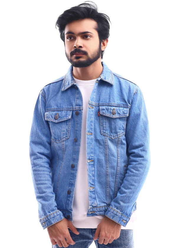 A man wearing a light blue denim jacket with a button-down front, chest pockets, and long sleeves. He has his arms crossed.