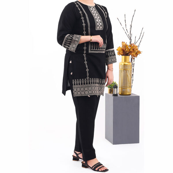 A front view of a Ladies Stitched Khaddar 2pc Set, showcasing a colorful embroidered kurta with matching pants, displayed on a hanger and draped over a wooden ladder.
