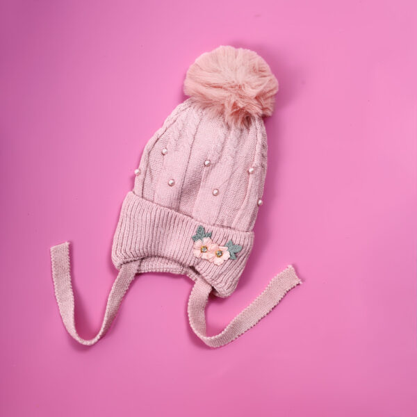Pink knit hat with a fluffy pom-pom, pearl embellishments, and floral applique, with ties
