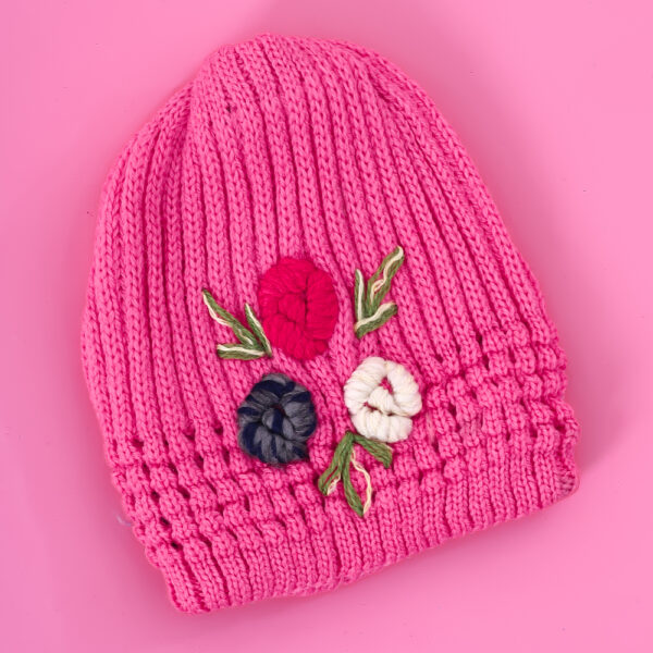 A hot pink knit beanie with a ribbed cuff and three embroidered abstract floral shapes in pink, grey, and white, with green and white leaves.